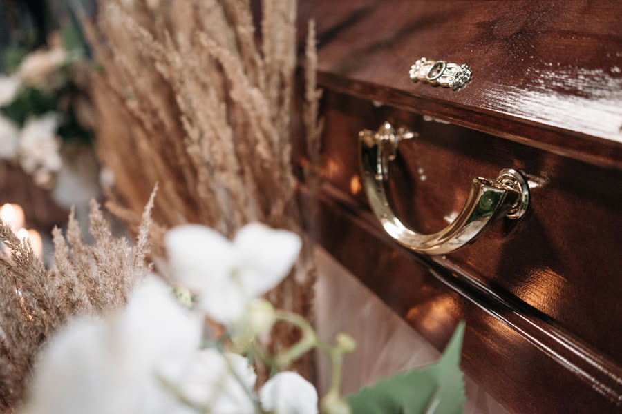 White flowers and dried flowers beside a wooden coffin